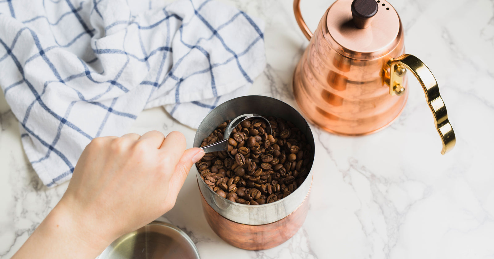 coffee being scooped from a copper canister with a copper hario v60 kettle behind it