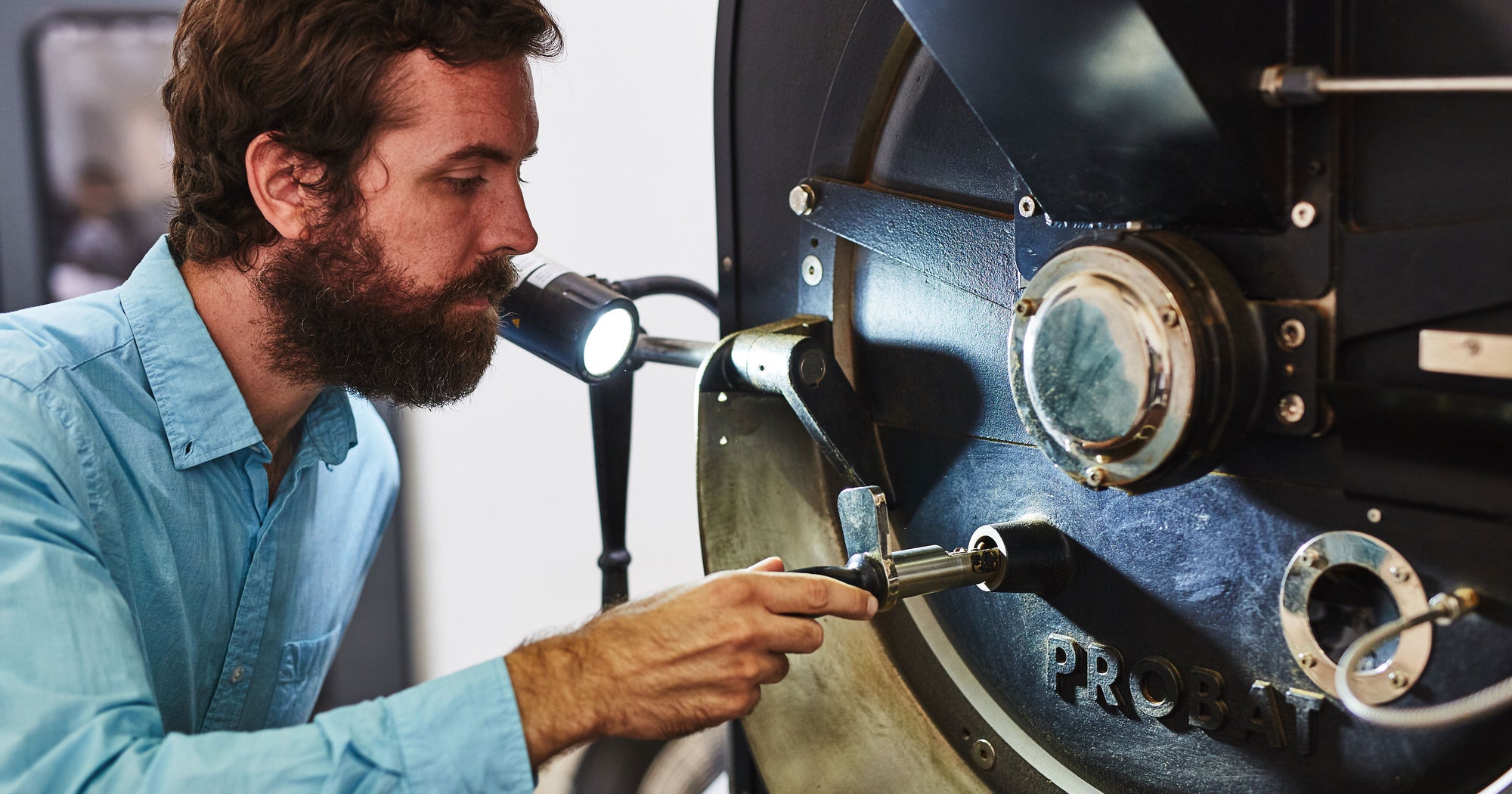 a bearded man roasting coffee on a probat coffee roaster