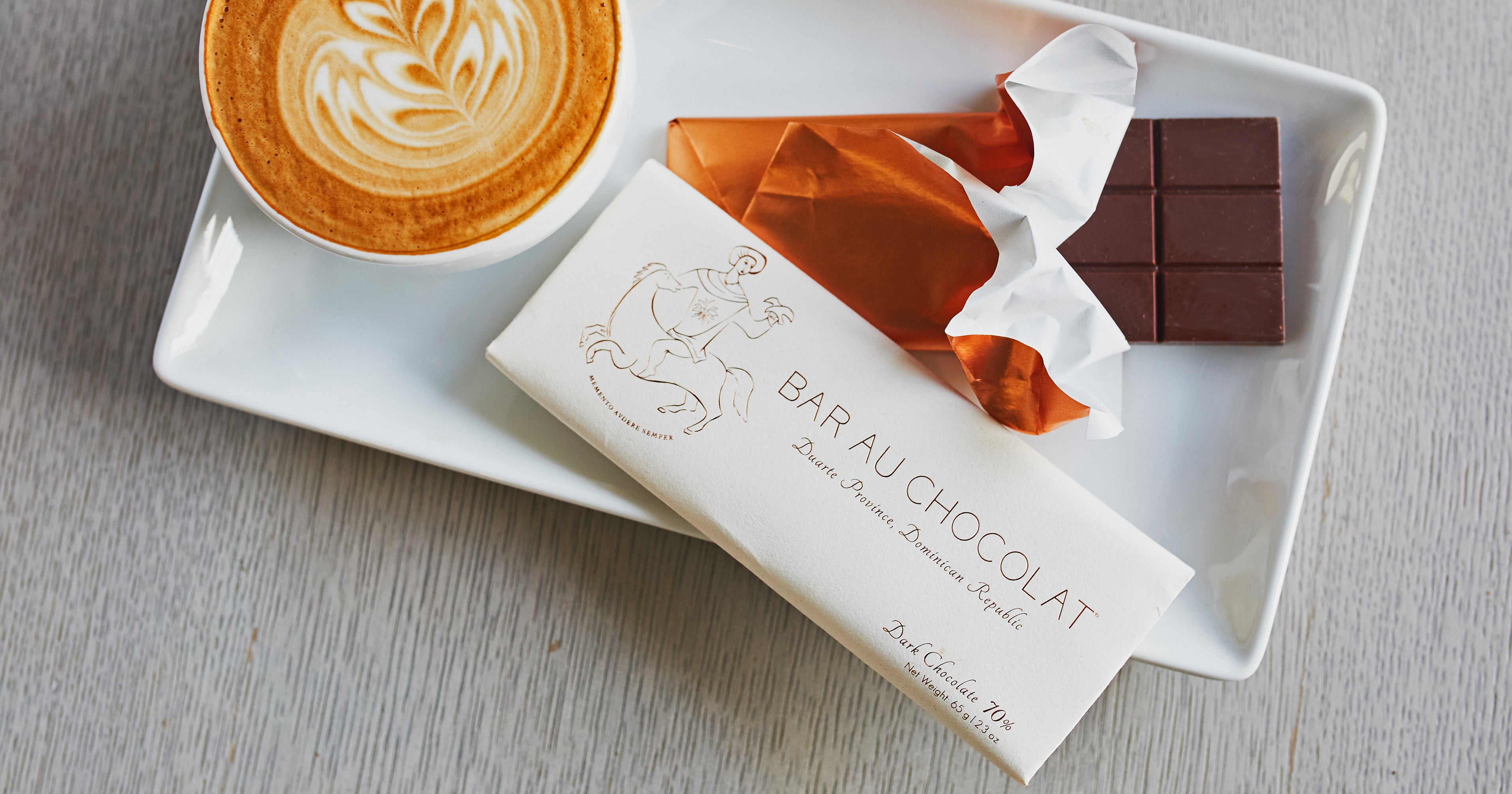 a partially unwrapped bar of chocolate next to a latte with rosetta latte art
