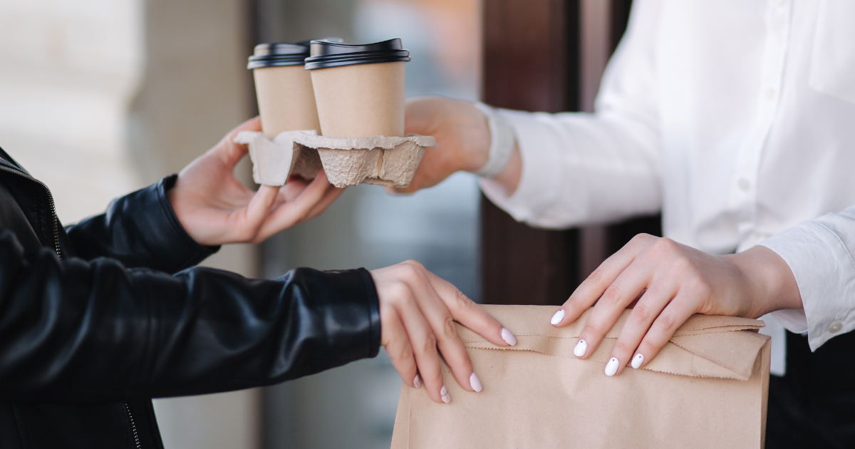 A person handing another person 2 to-go coffees and a paper bag of caffe goodies.