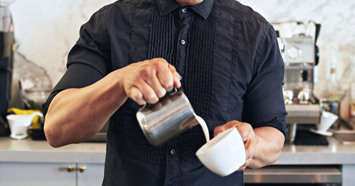 Caffe Luxxe barista pouring cream into a cup of coffee