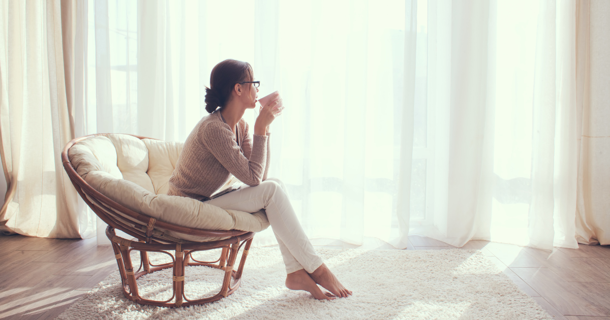 Woman sitting in a cozy chair by a large window, enjoying her morning cup of coffee.