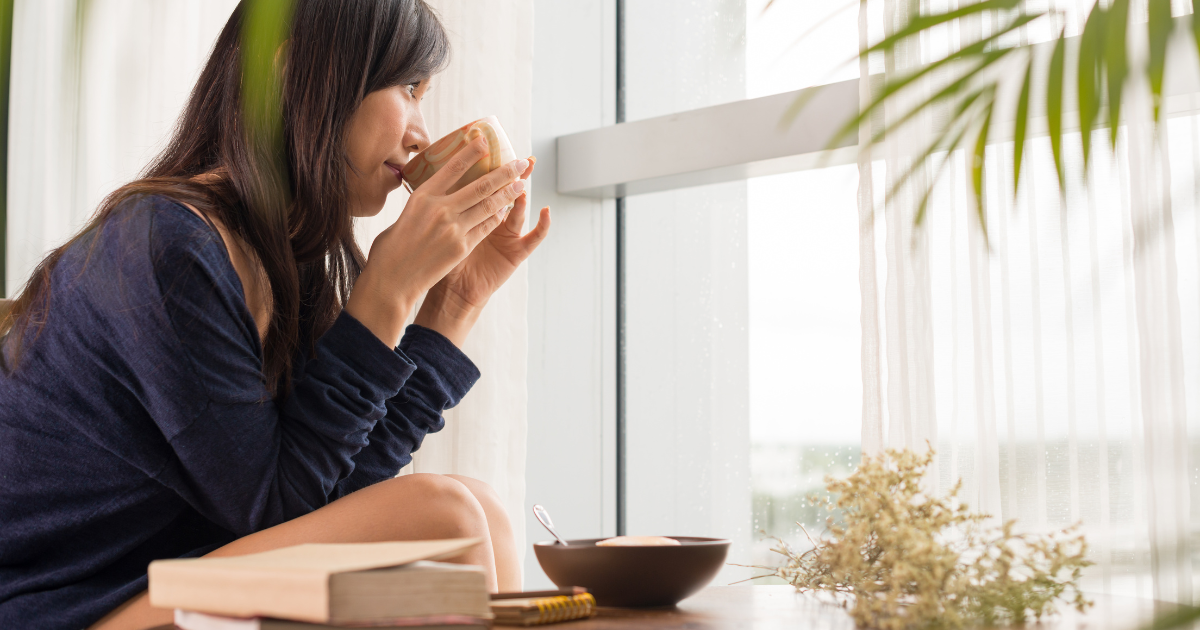 Woman drinking coffee calmly while enjoying the view out her window.