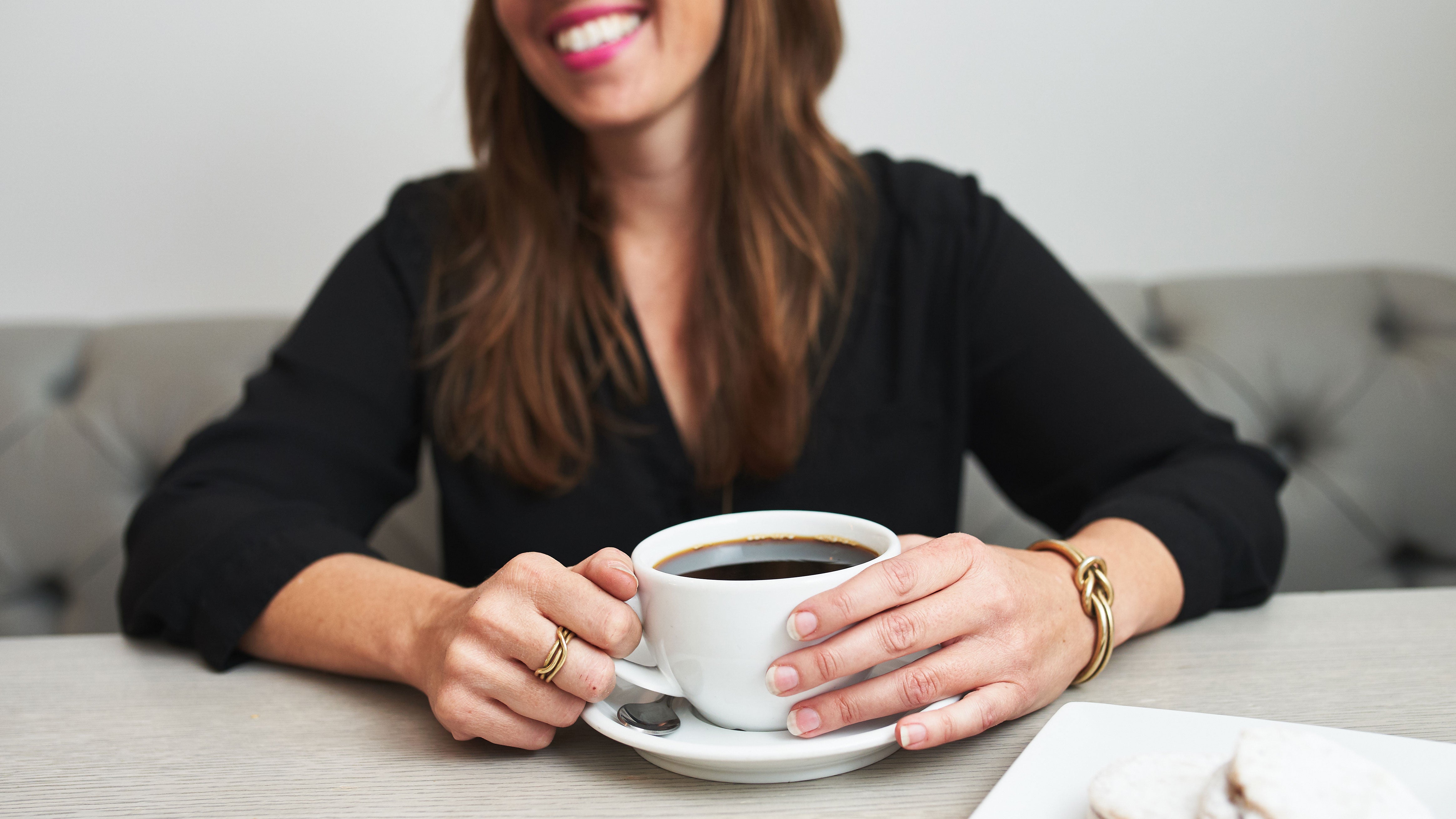 a woman smiling while holding a cup of black coffee