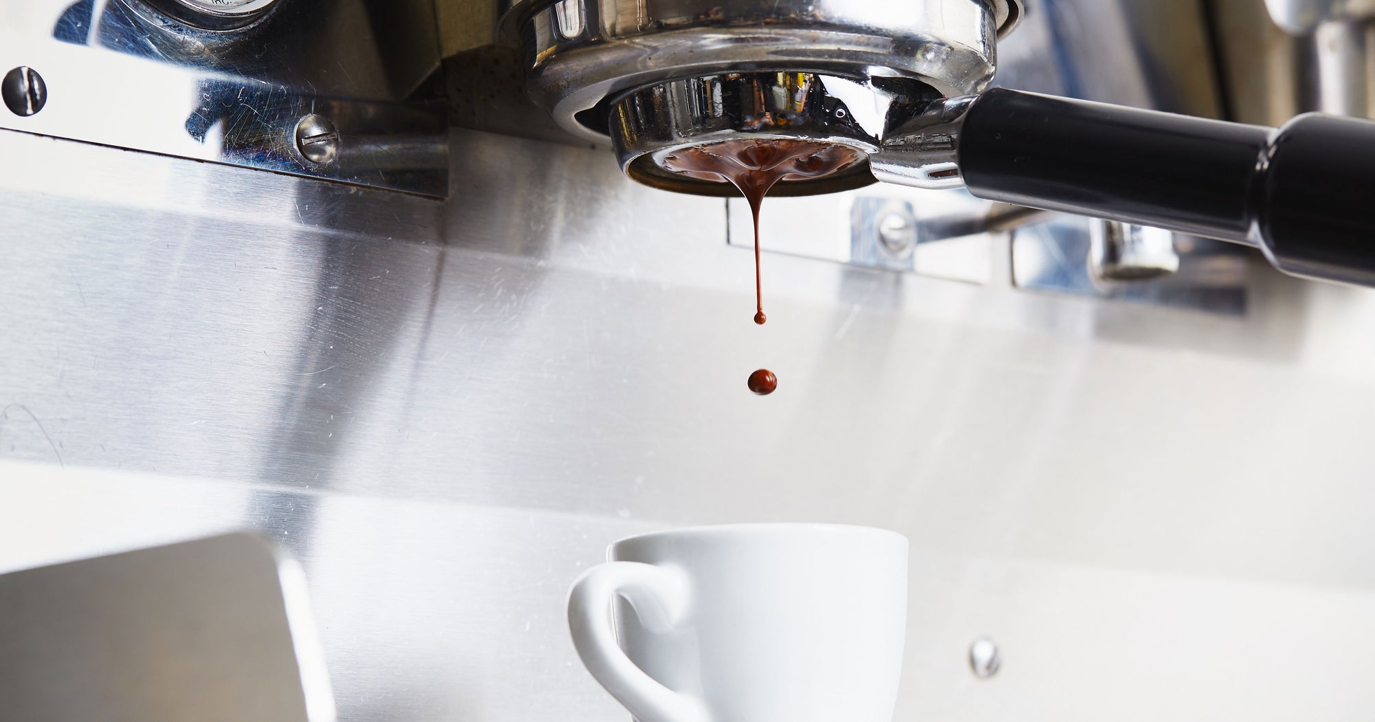 espresso being extracted from a bottomless portafilter into a white demitasse