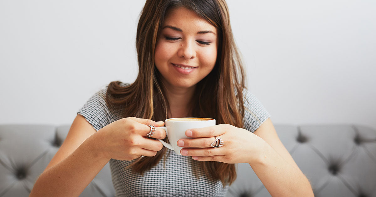 a woman smiling at and holding a cup of coffee