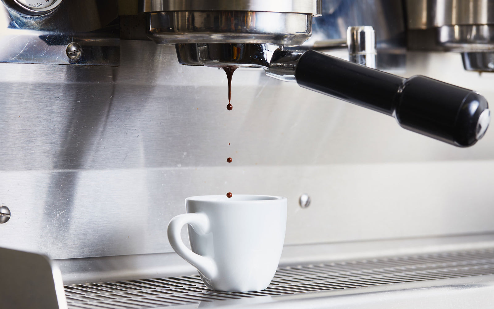 espresso being brewed from a bottomless portafilter into a small white demitasse