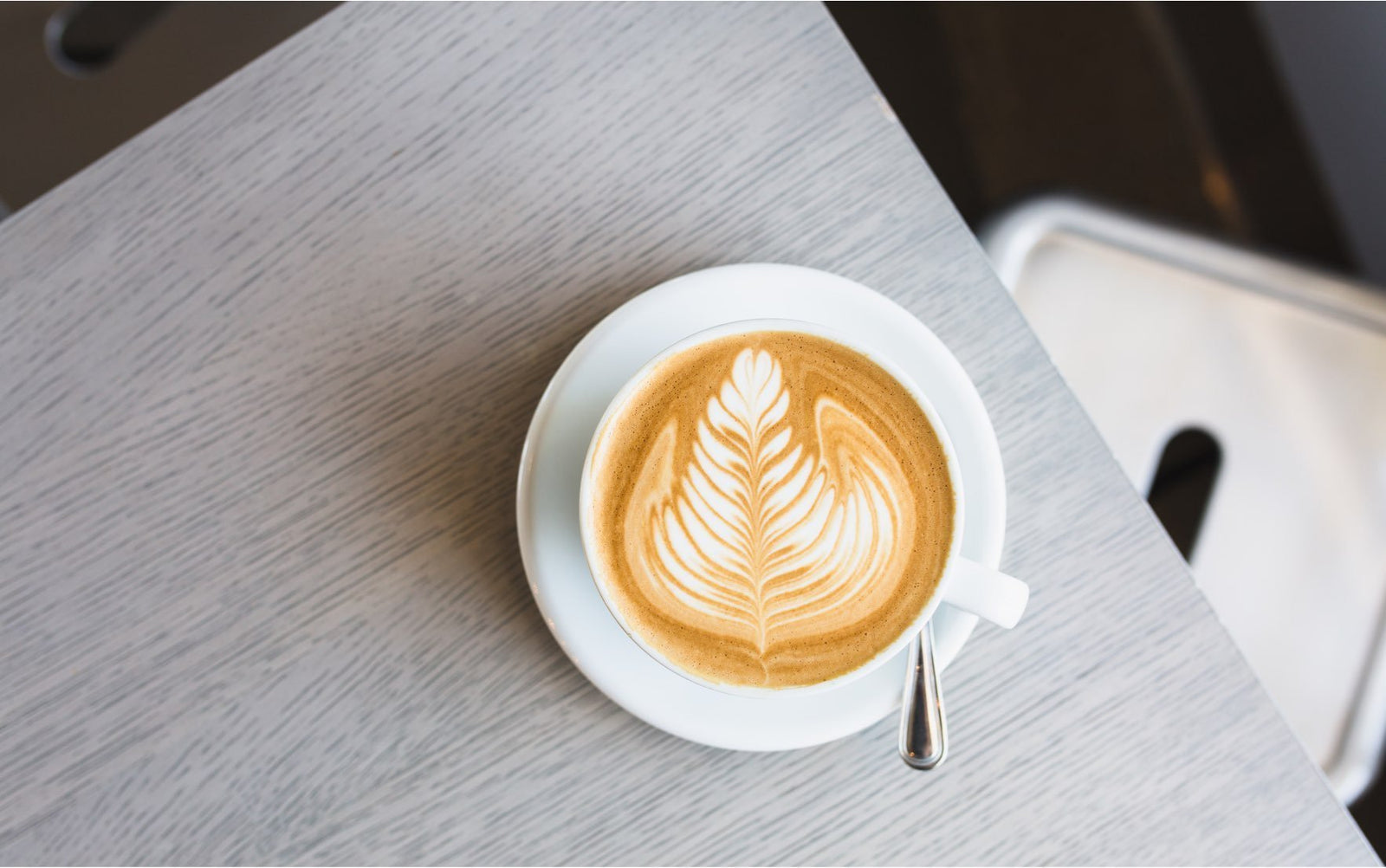 a latte shot from above with rosetta latte art. the latte sits in on a saucer, which in turn sits on a grey table.