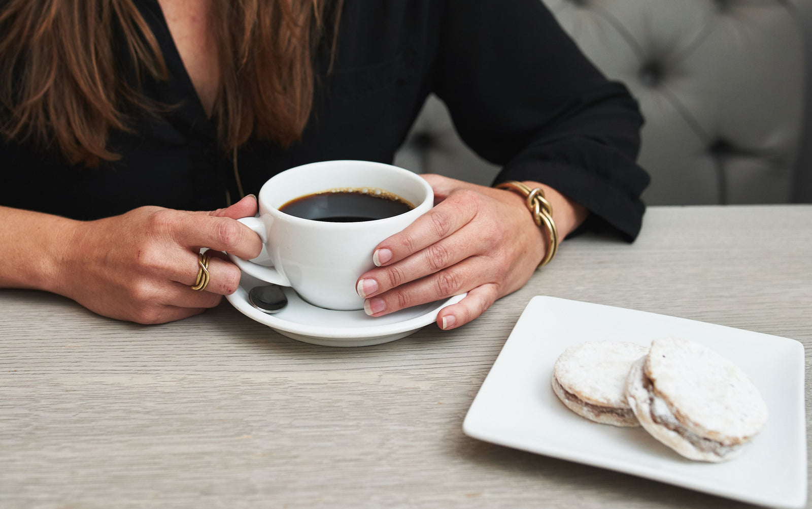 a seated person holding a cup of coffee in front of them with alfajores in the foreground