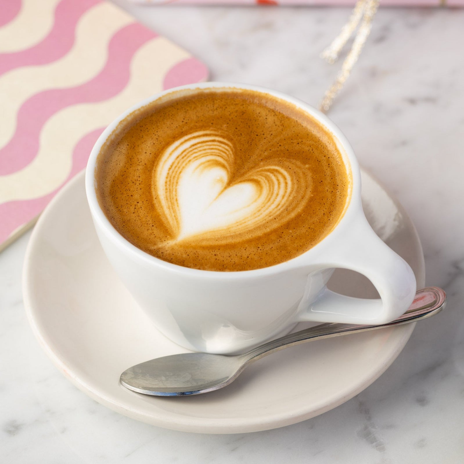Cappuccino with heart foam on a marble surface with strawberries and a gift box.