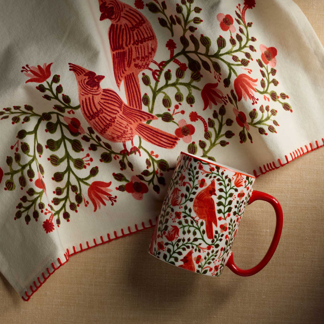 Red mug and decorative cloth with bird and floral pattern on a beige surface